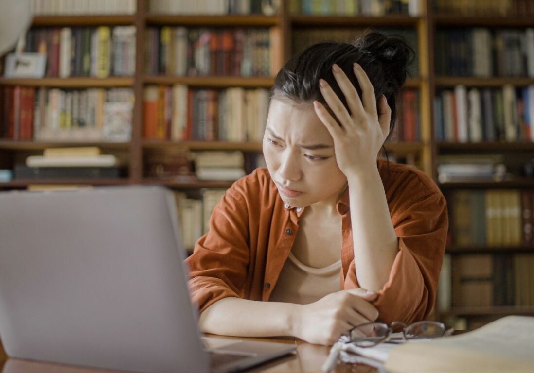 Photo of a woman looking forlorn at her laptop.