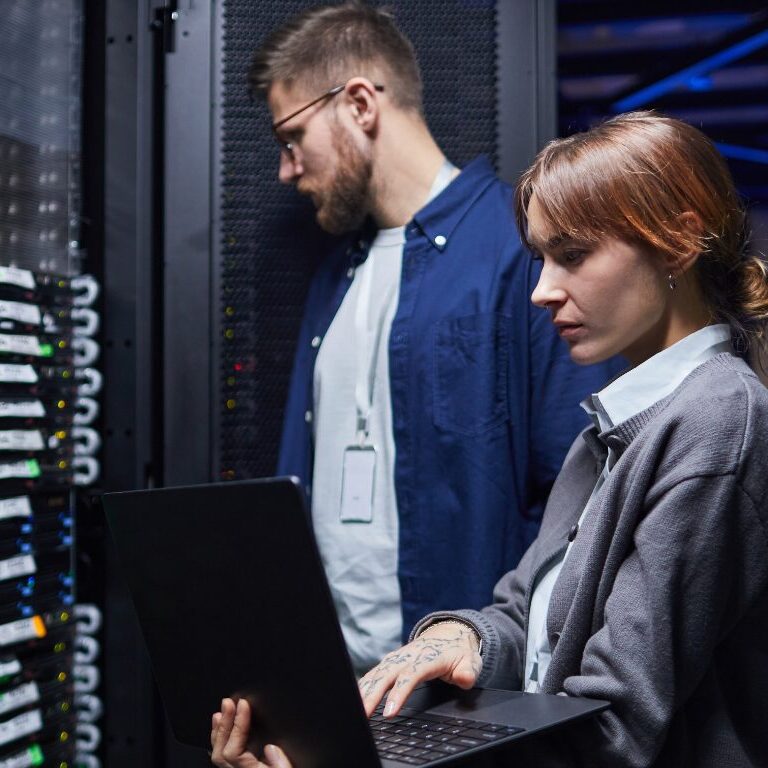 Man looking at network servers and a woman holding a laptop typing.